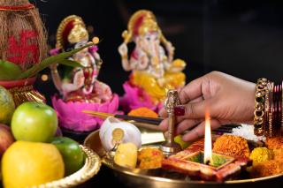 a person touches a Ghanti bell on a Hindu altar, in front of statues of Ganesha and Lakshmi 
