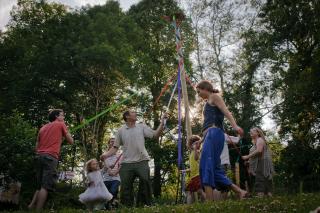 People of many ages dance around a maypole in spring.