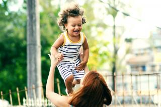 A toddler laughs, mid air, as an adult lifts the toddler into the air.