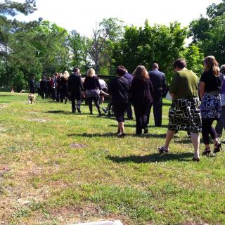 A group of mourners walks across a cemetery green.