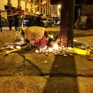 At the base of a street sign, a collection of small candles and flowers to honor victims of a terrorist bombing