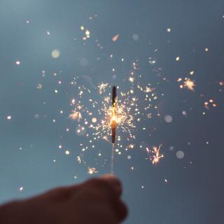 Against a dim sky, a hand holds a lit sparkler